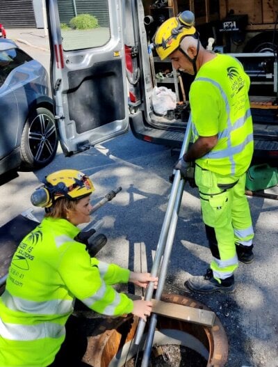 To personer i signalfargede verneklær er på vei ned i en kum. Foto: Ruden AS